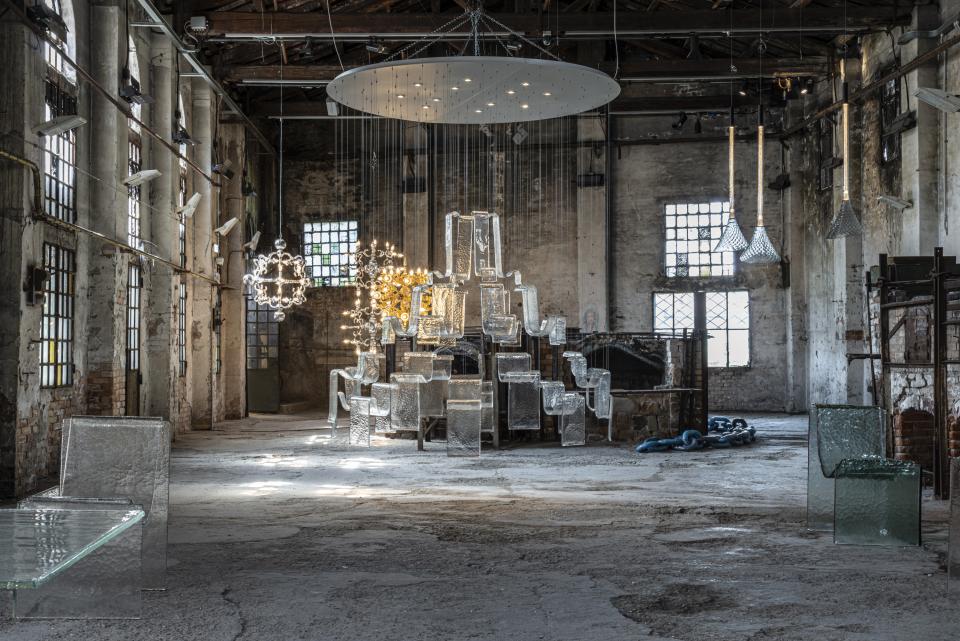 Clear glass furniture and lighting installations showcased in a rustic industrial space at the GLASS to GLASS exhibit.