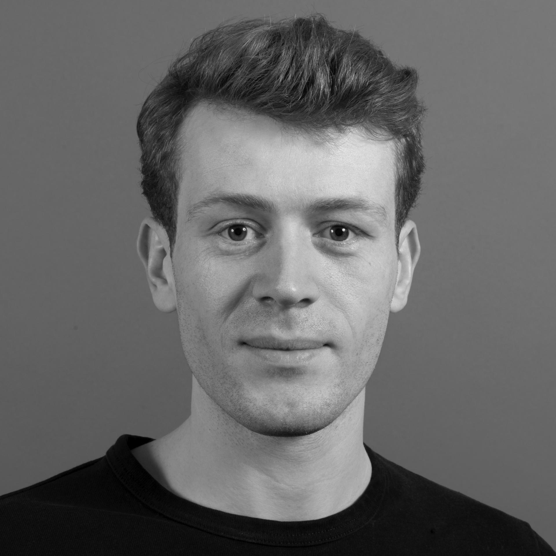 A man with short hair and a black shirt poses against a simple gray background, representing innovative architecture research.