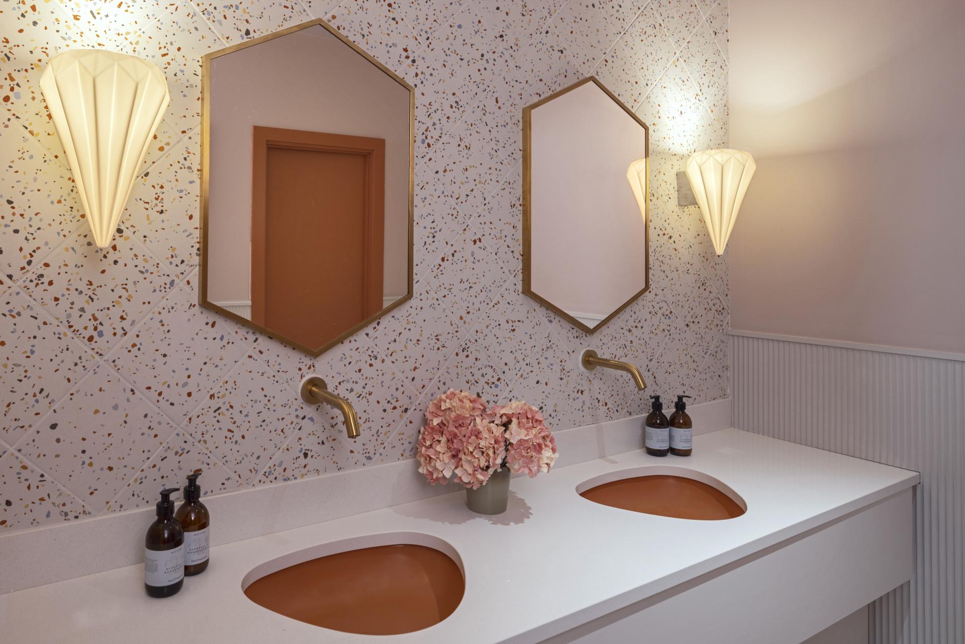 Stylish bathroom featuring hexagonal mirrors, elegant lighting, and a dual sink with a unique terracotta basin.