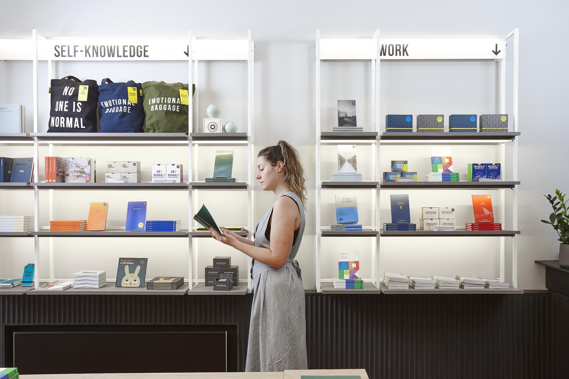 A woman browses a colorful bookshelf filled with books and bags, reflecting modern design in East London.