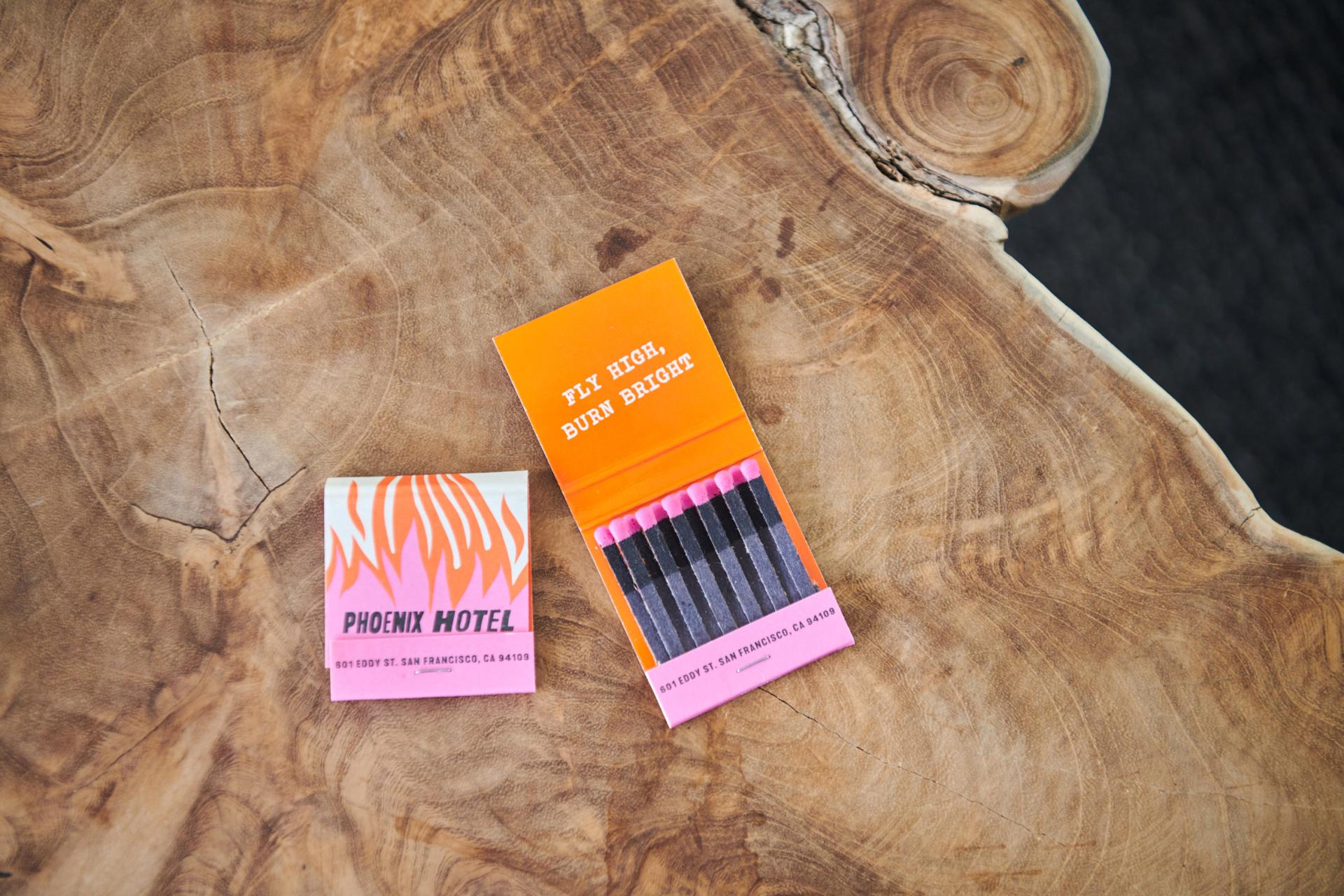 Colorful matchbooks for the Phoenix Hotel on a wooden surface, showcasing its stylish branding and playful slogan.