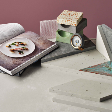 Assorted quartz surfaces and an open design book feature intricate textures and a gourmet dish, highlighting interior design trends.