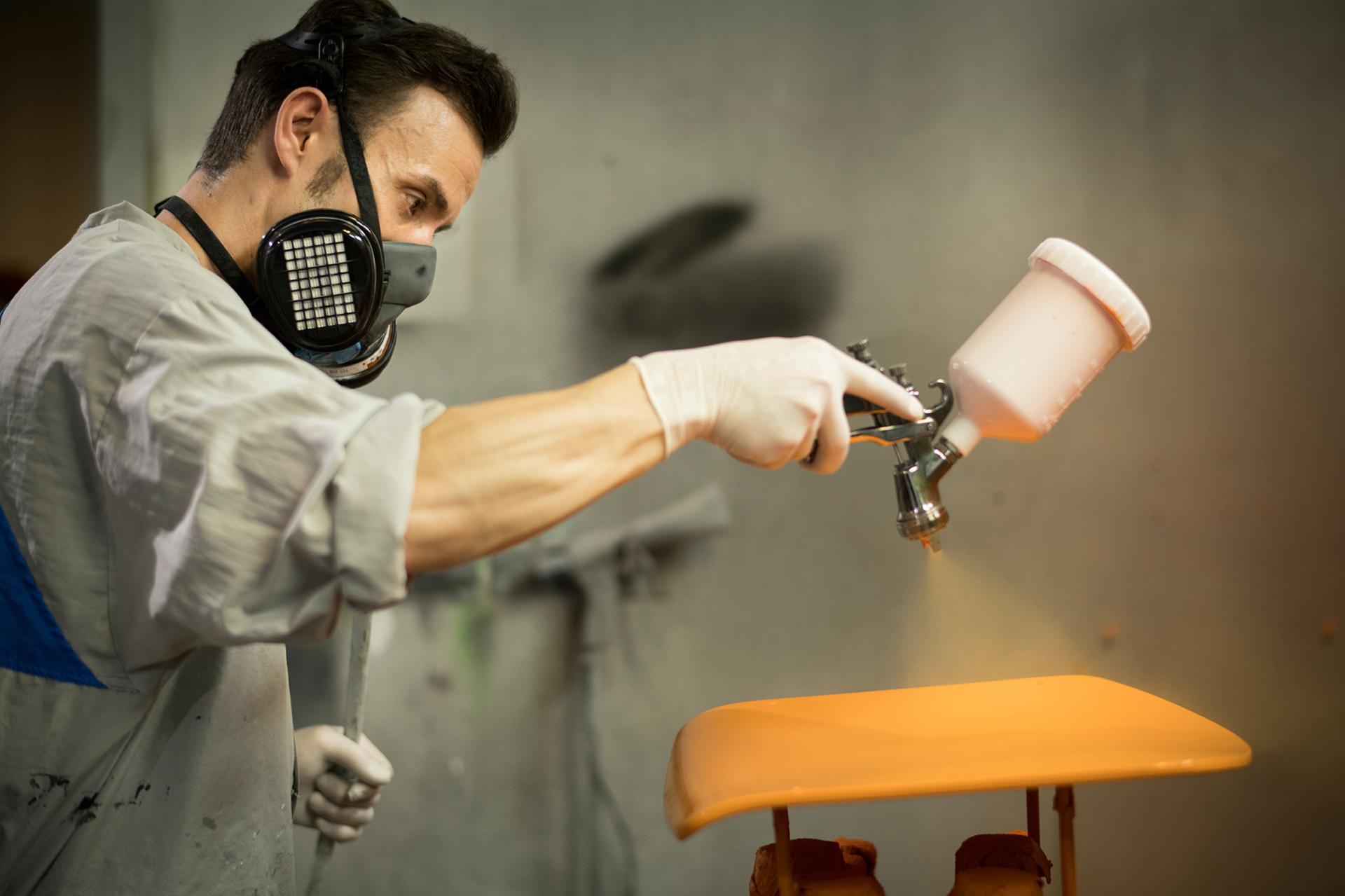 A worker spray-painting a vibrant orange surface in Thonet's production facility, highlighting short supply chains in Germany.