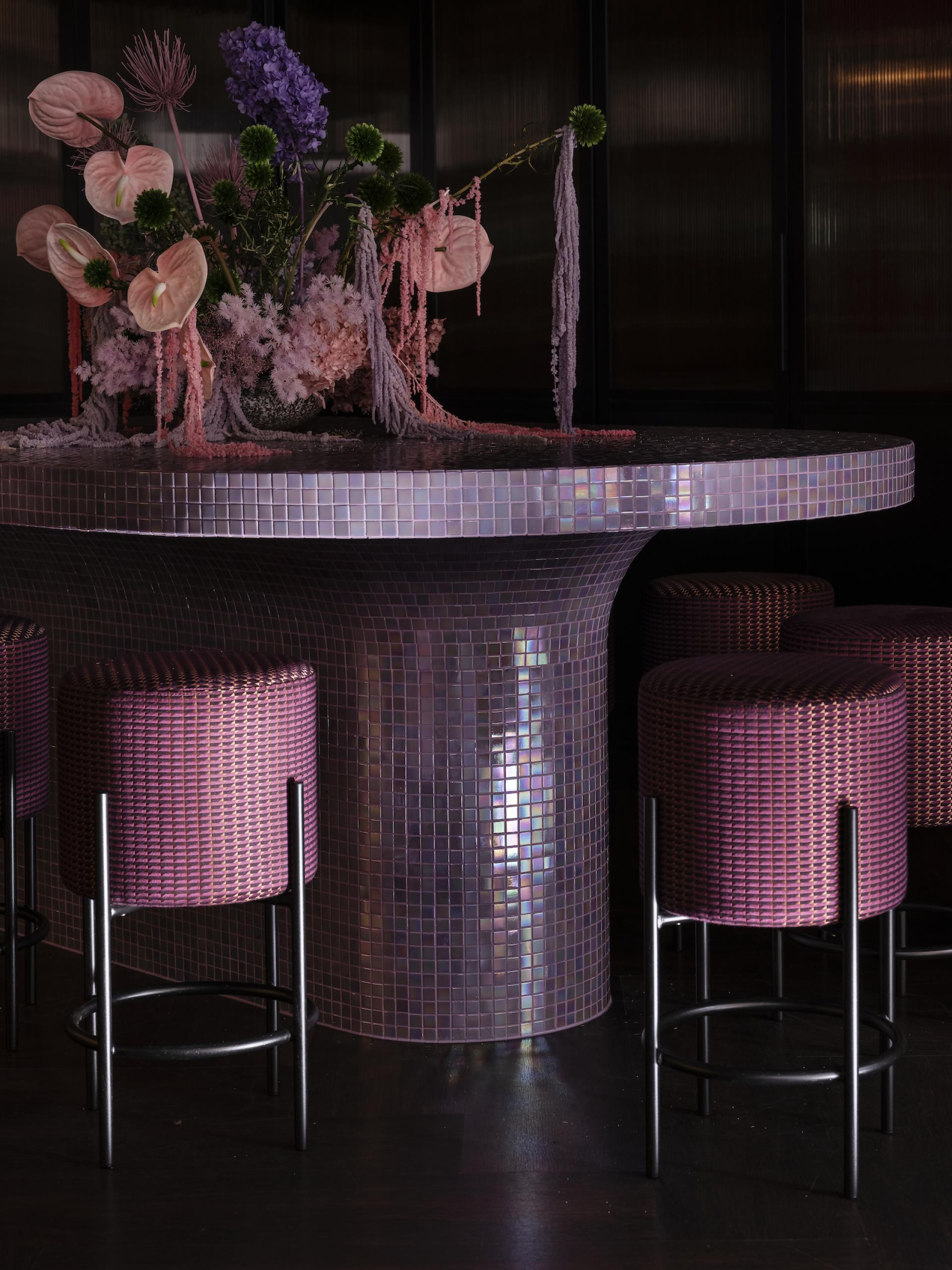 Vibrant floral arrangement atop a mosaic bar, featuring pink anthuriums and purple blooms in the stylish Naumi Studio Hotel.