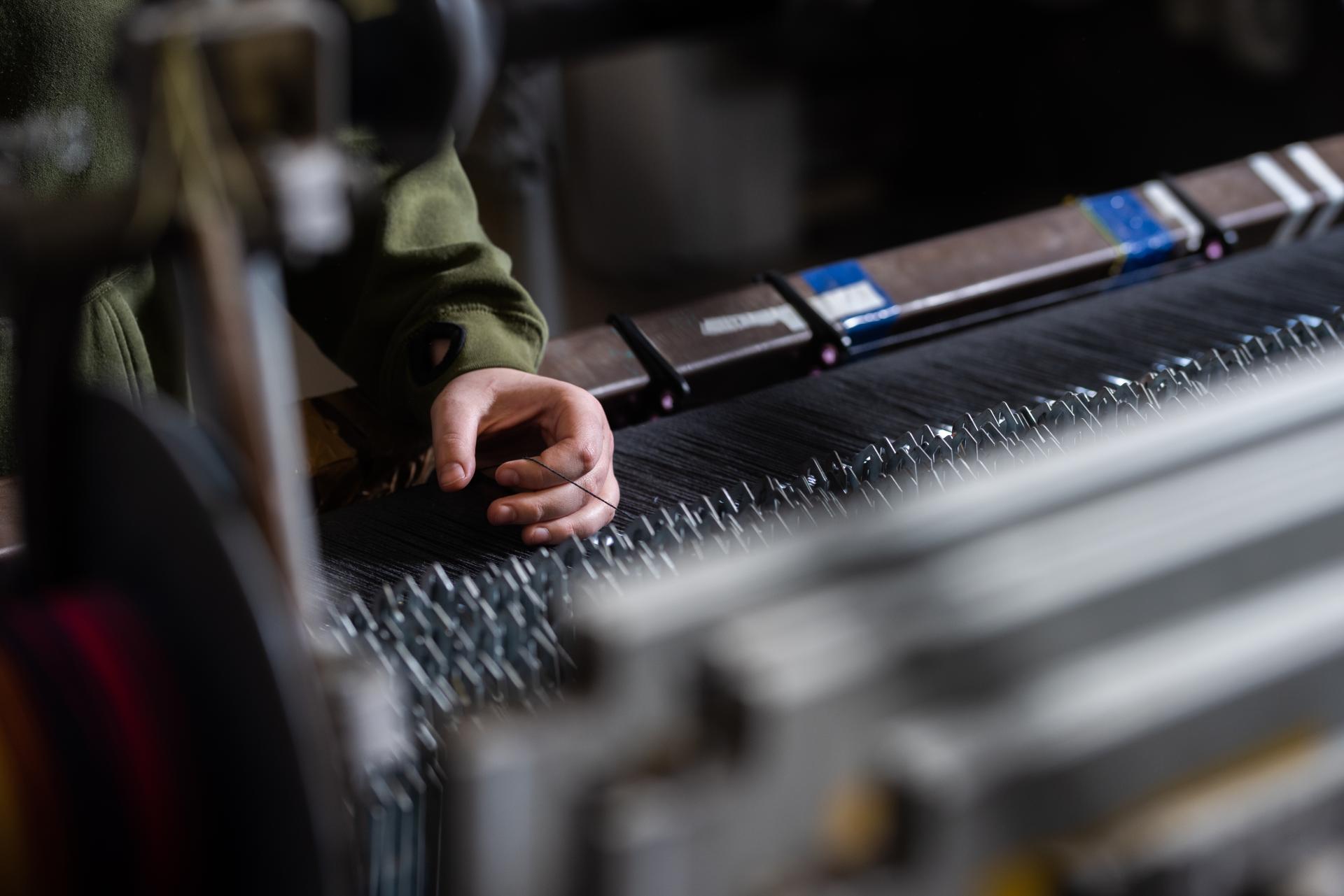 Hand adjusting threads on a weaving machine, showcasing traditional manufacturing techniques at Bute, a historic textile mill.