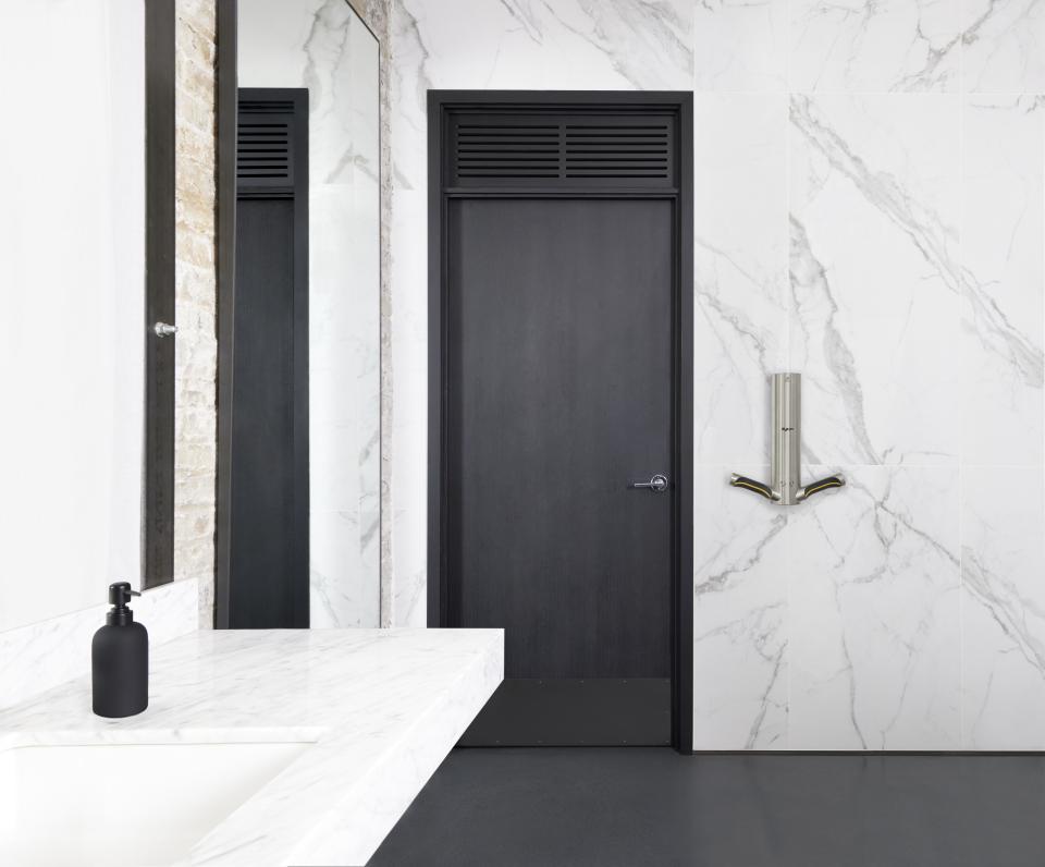 Modern bathroom featuring a sleek marble wall, minimalist sink, and a stylish Dyson hand dryer, emphasizing sustainable design.
