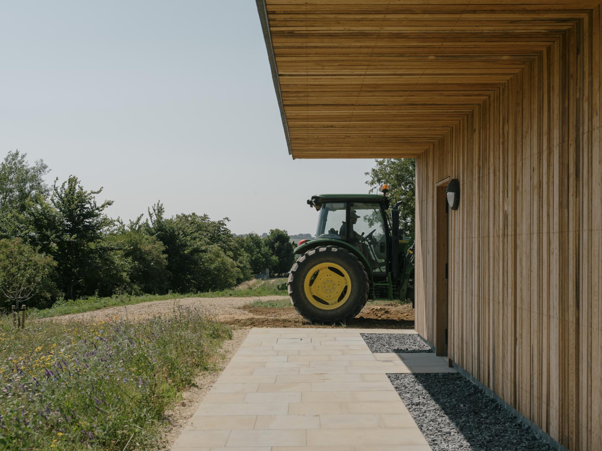 Regenerative farming centre in the Cotswolds featuring a tractor and sustainable architecture amidst lush greenery.