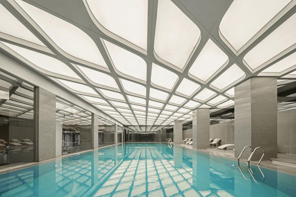 Elegant indoor swimming pool with modern design, illuminated ceiling, and reflective water surface, part of the Rhythm community centre.