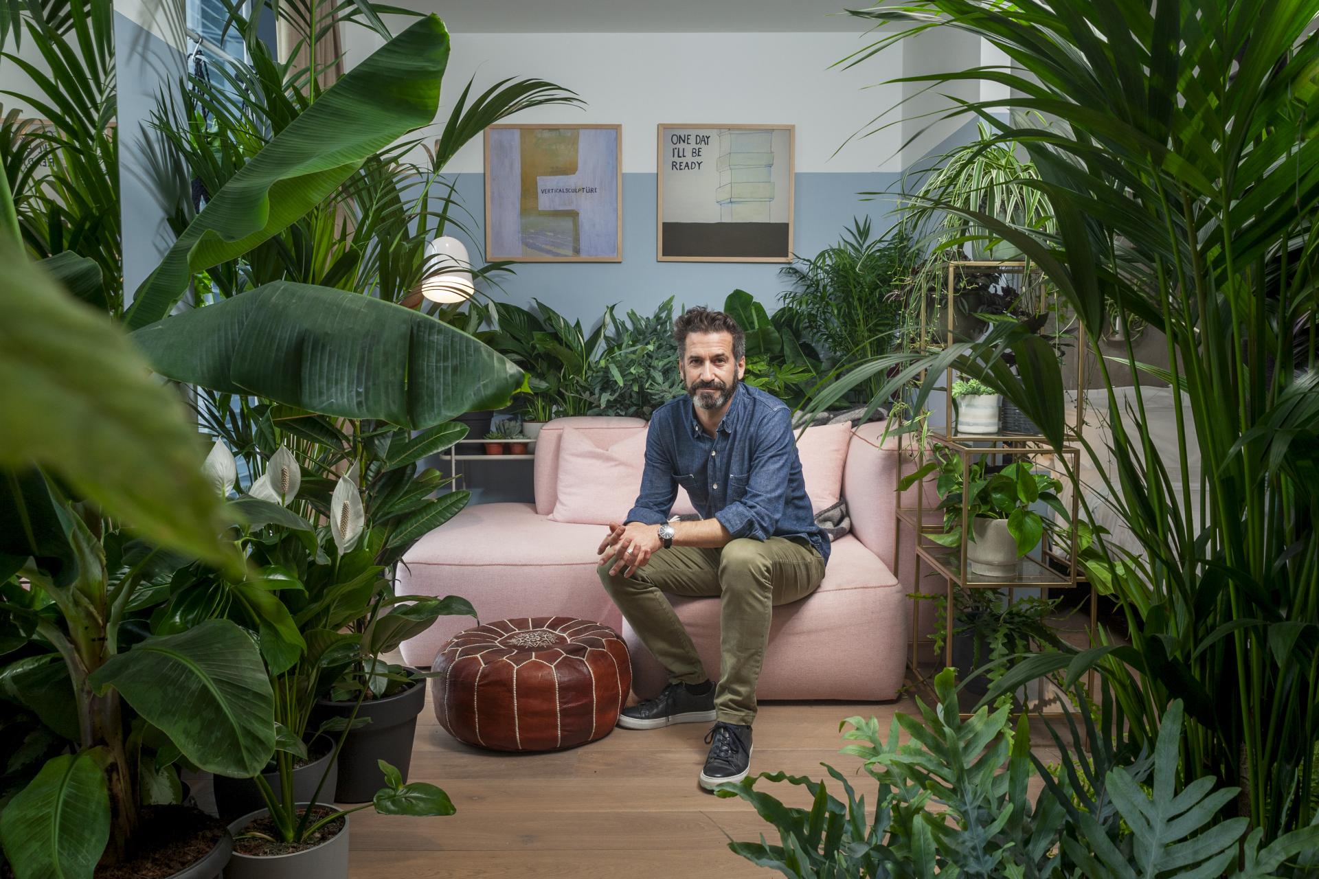 Modern living space surrounded by lush plants, featuring a man seated on a pink couch, highlighting nature in design.