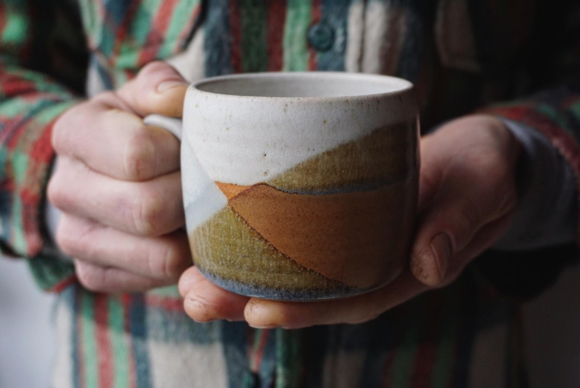Handcrafted ceramic mug with earthy tones held by a person, showcasing creative craft in Bristol.