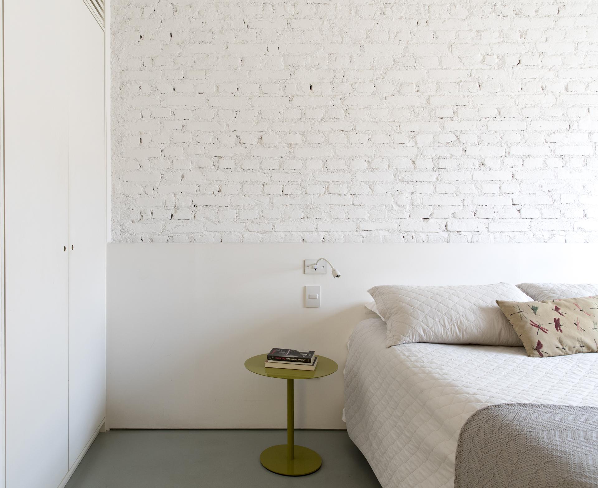 Renovated 1950s bedroom featuring a white brick wall, minimalist decor, and vibrant green side table in São Paulo.