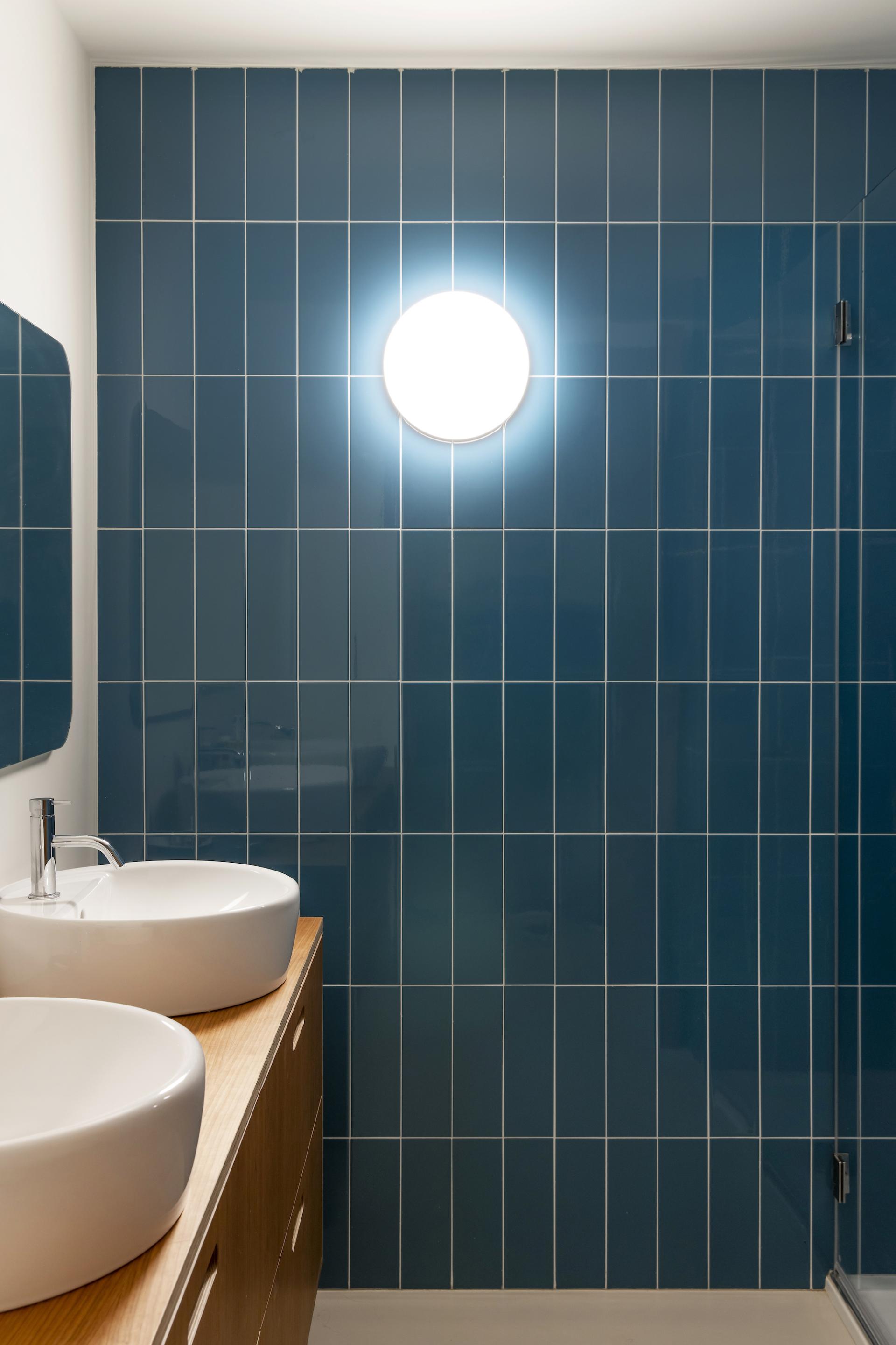 Modern bathroom featuring stylish blue ceramic tiles, circular light fixture, and sleek sink design, highlighting Spanish ceramic design innovation.