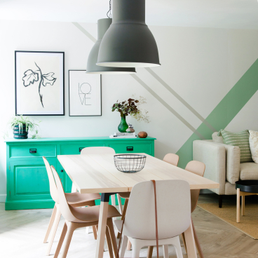 Stylish dining area featuring Scandinavian industrial design, green sideboard, modern light fixtures, and minimalist decor elements.