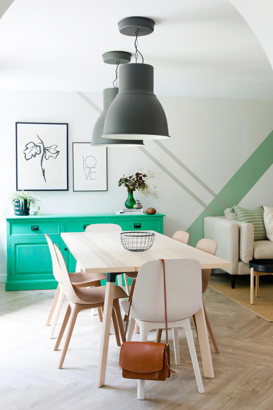 Stylish dining area featuring Scandinavian industrial design, green sideboard, modern light fixtures, and minimalist decor elements.