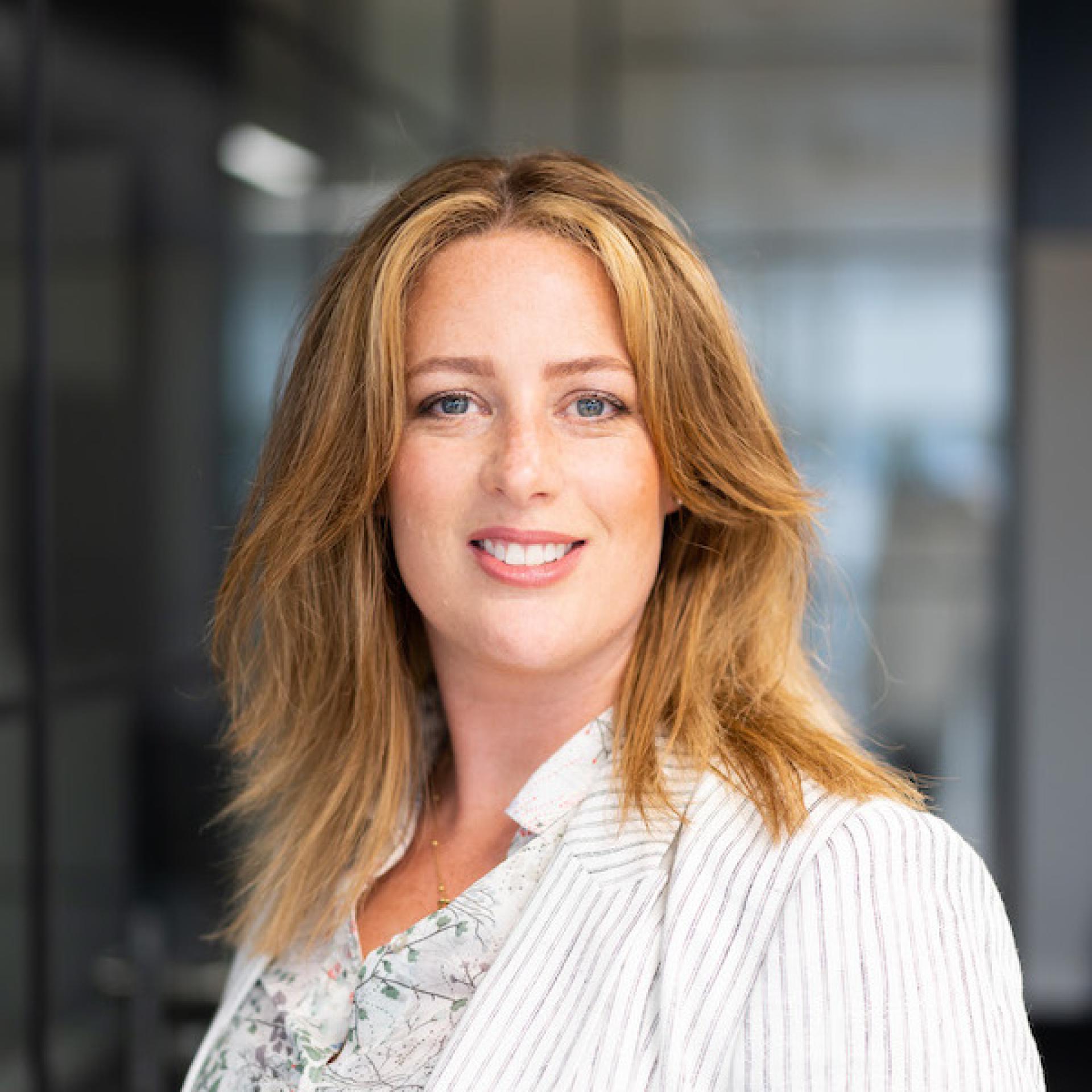 Smiling professional woman with long hair, wearing a striped blazer, in a modern office setting, emphasizing workplace technology.