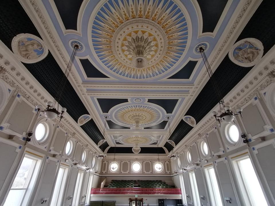 Refurbished ballroom ceiling of Todmorden Town Hall featuring intricate moldings, decorative patterns, and elegant lighting.