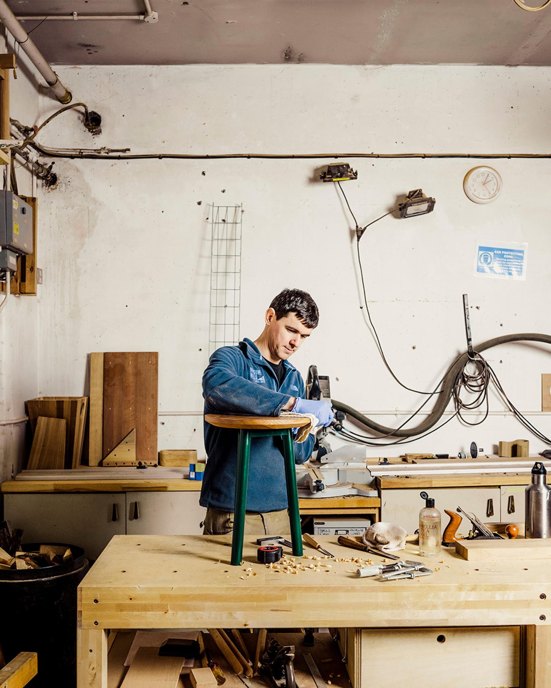 Craftsman working on a wooden stool in a workshop, showcasing craftsmanship related to Material Matters at London Design Festival 2023.