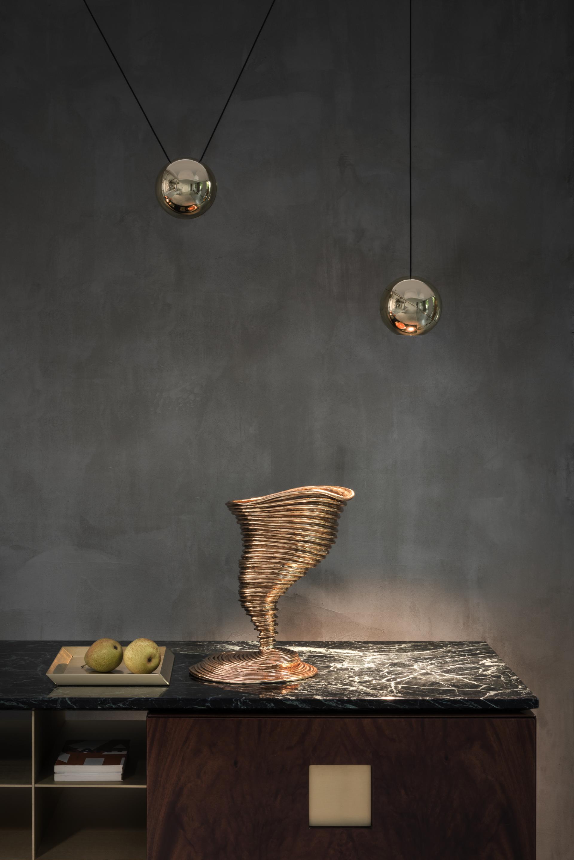 Brass decorative sculpture by GHIDINI 1961 on a marble countertop, with hanging light fixtures and green apples.