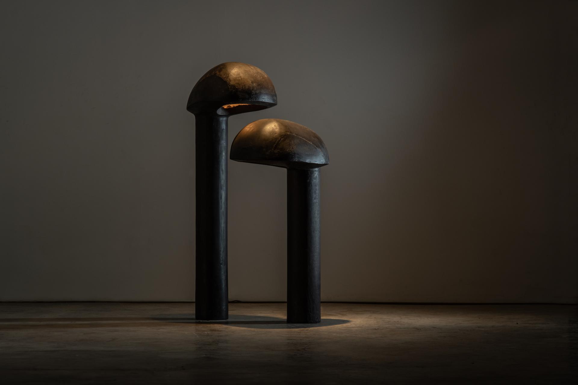 Abstract sculptures featuring two cylindrical forms with domed tops, illuminated in a gallery setting for the Reynold Rodriguez solo show.