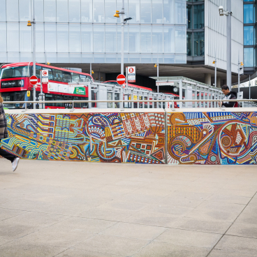 Vibrant mural showcasing traditional craft and community diversity, with pedestrians and red buses in an urban setting.