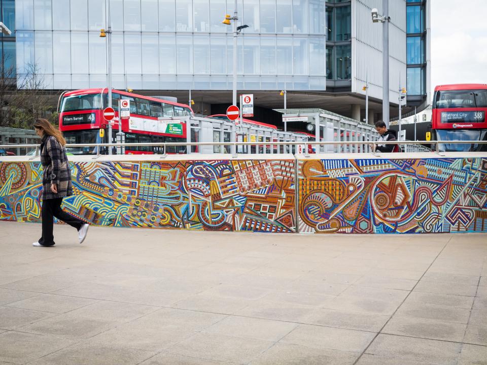 Vibrant mural showcasing traditional craft and community diversity, with pedestrians and red buses in an urban setting.