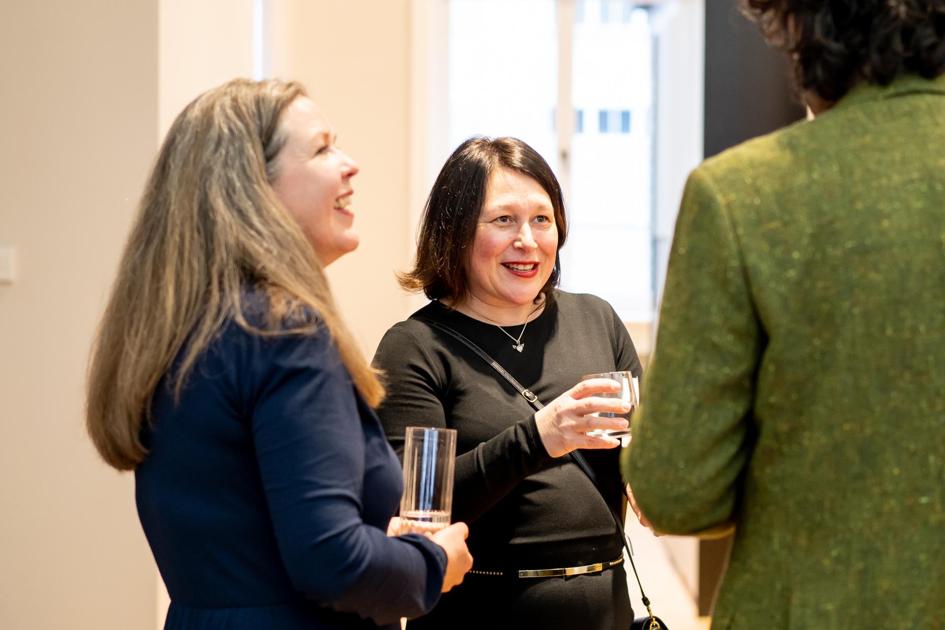 Two women engaged in conversation while holding drinks at a sustainability seminar event focused on combating climate change.