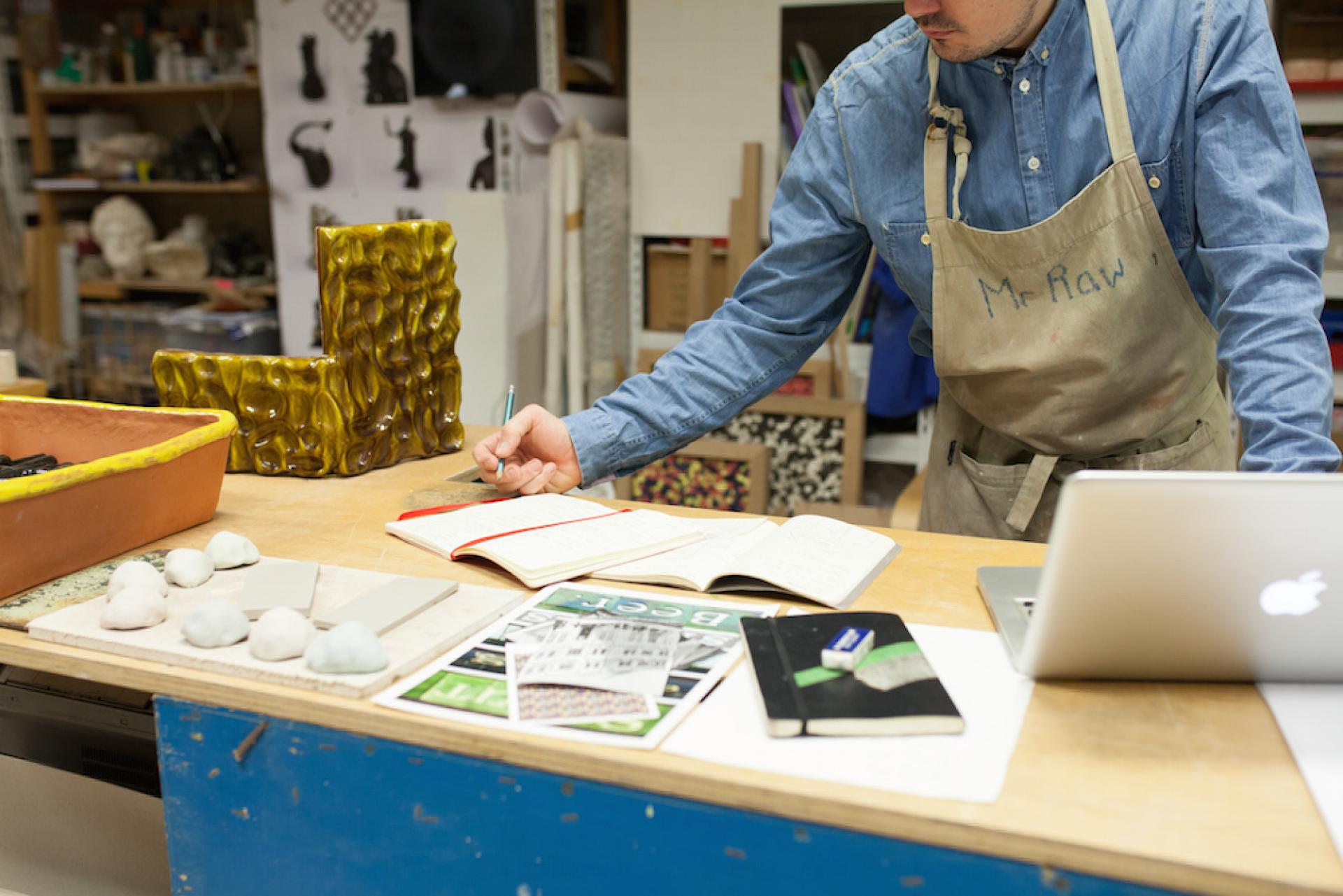 Ceramic artist Matthew Raw working in his studio, surrounded by clay pieces, notes, and materials for his creative process.