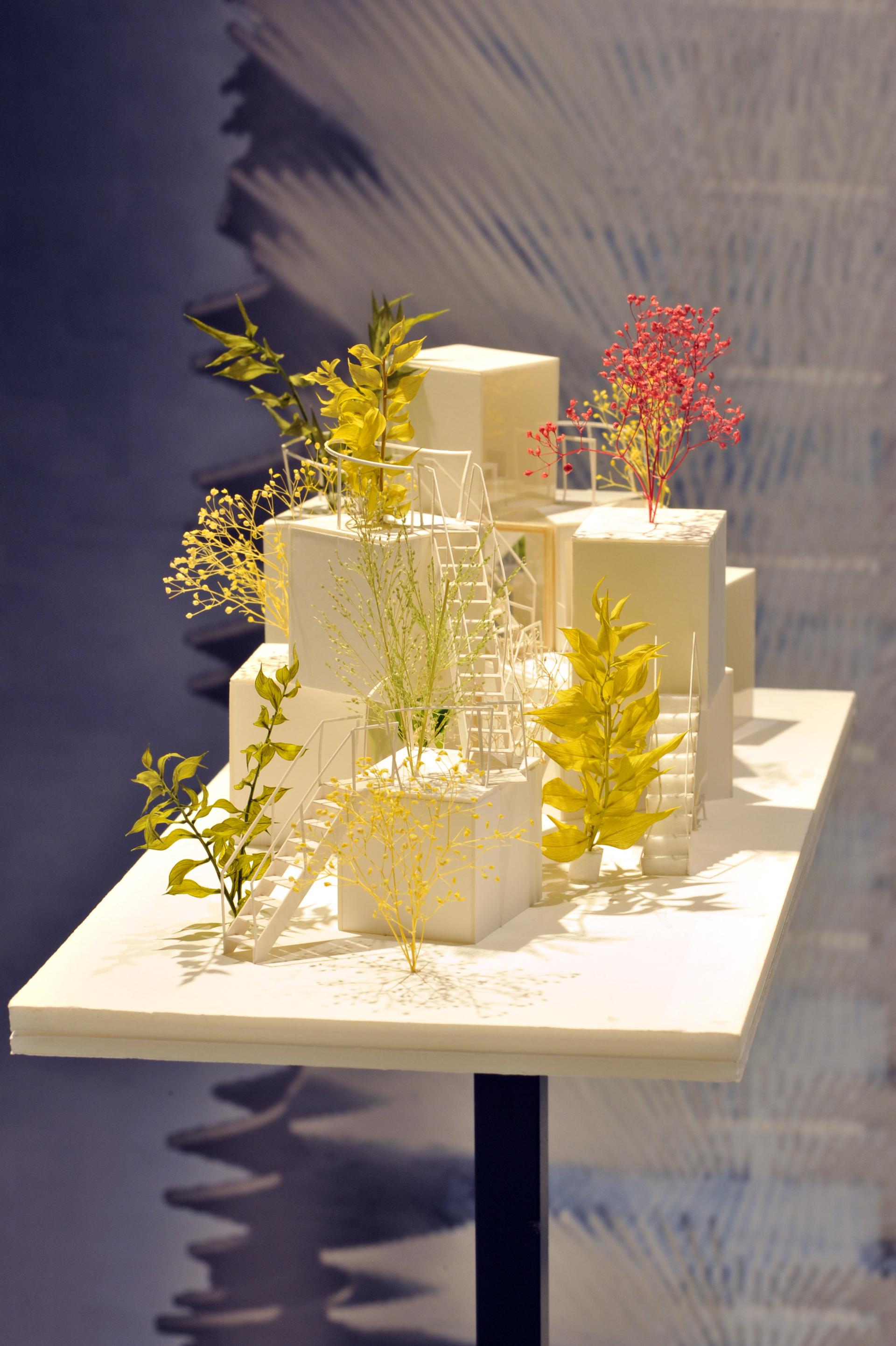 Architectural model featuring white structures adorned with vibrant plants, showcased at Sou Fujimoto's exhibit in Japan House London.