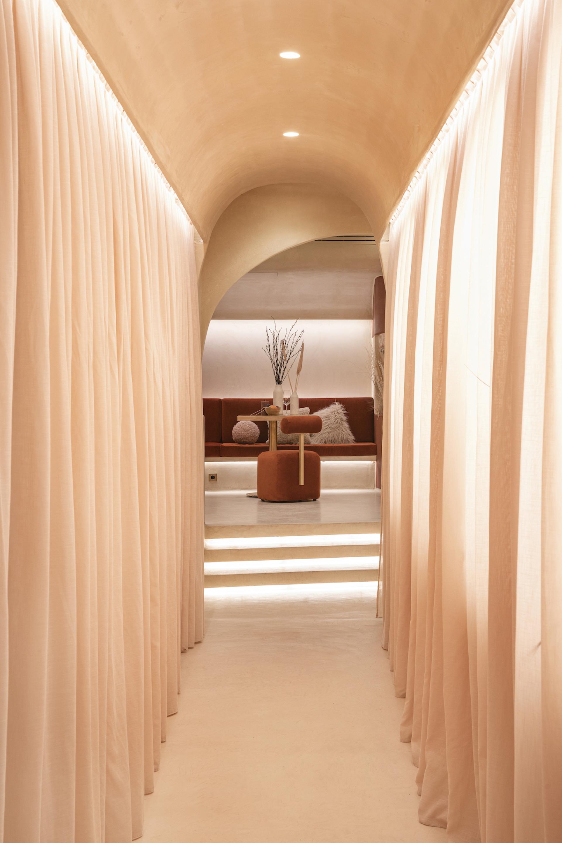 A warm, inviting corridor with soft curtains leading to a stylish seating area in the Living Bakkali restaurant.