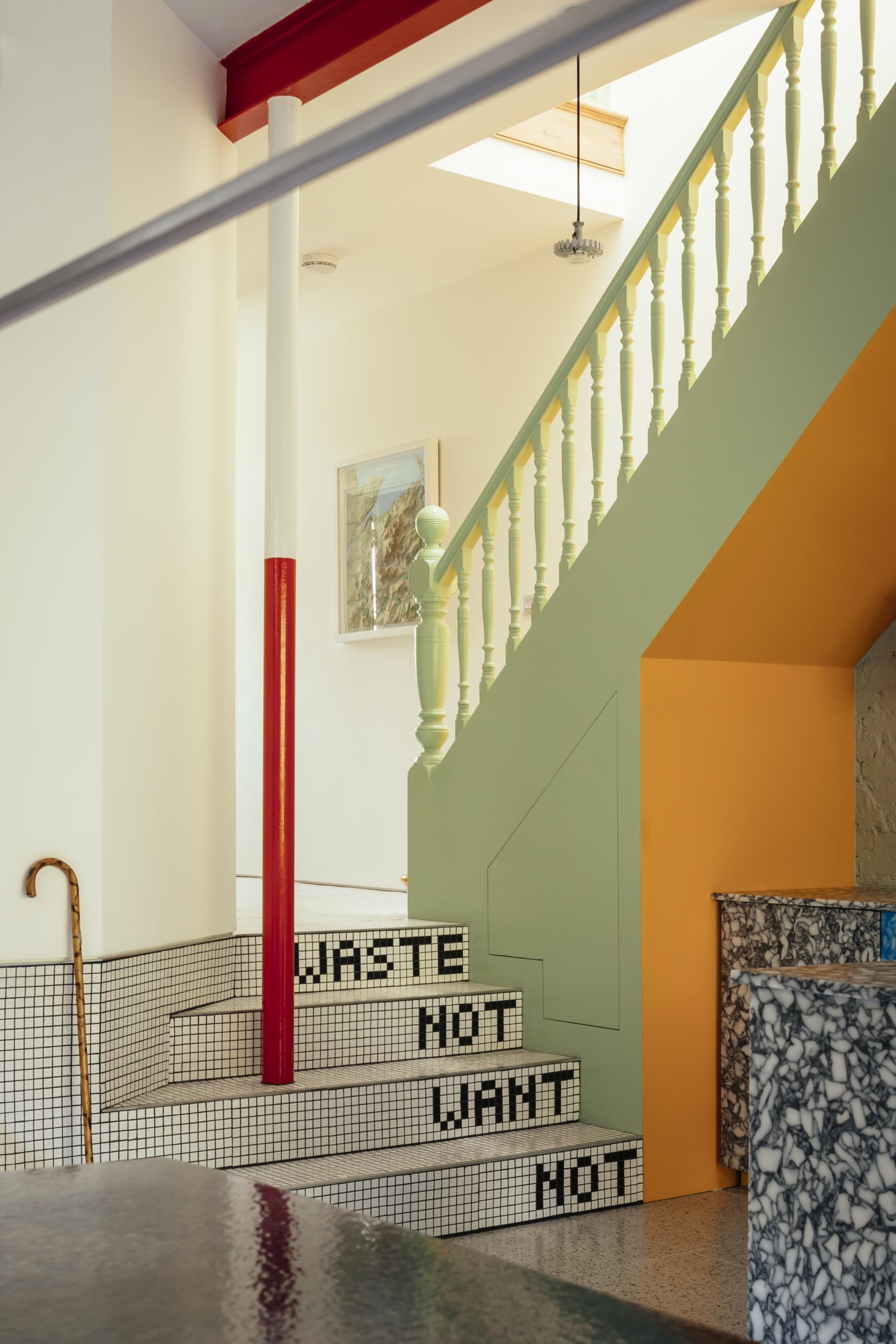 Colorful interior of an Edwardian home, featuring unique staircase design with a mosaic saying "WASTE NOT WANT NOT."