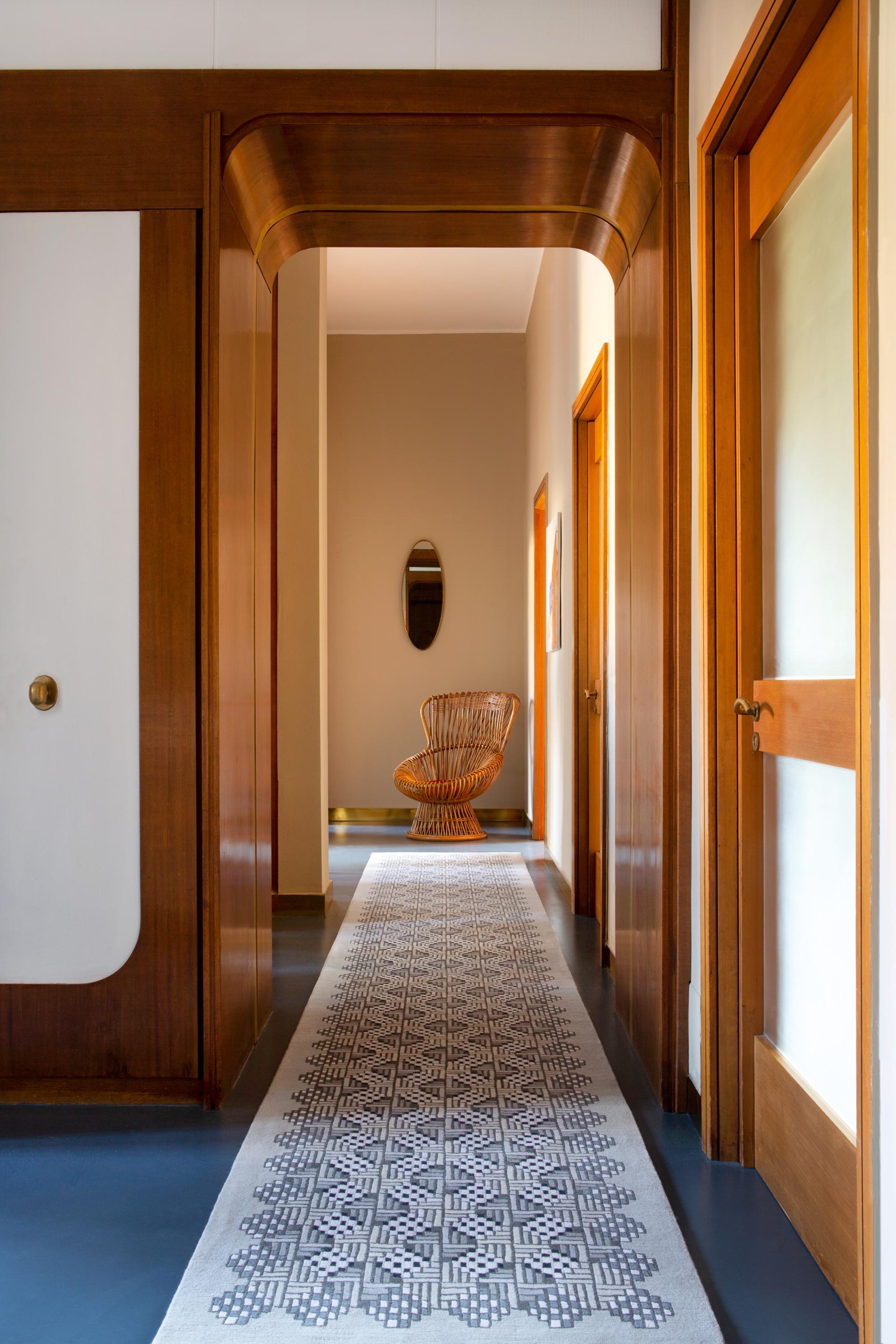 A stylish hallway featuring a patterned rug, wooden doors, and a unique wicker chair, reflecting contemporary interior design.