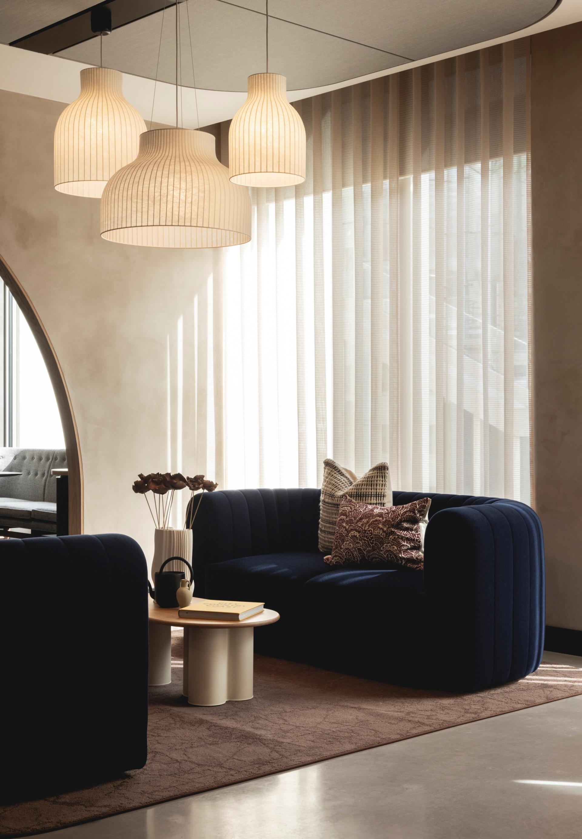 Elegant Art Deco-inspired lounge featuring curved navy sofas, decorative cushions, stylish pendant lights, and a calming atmosphere.