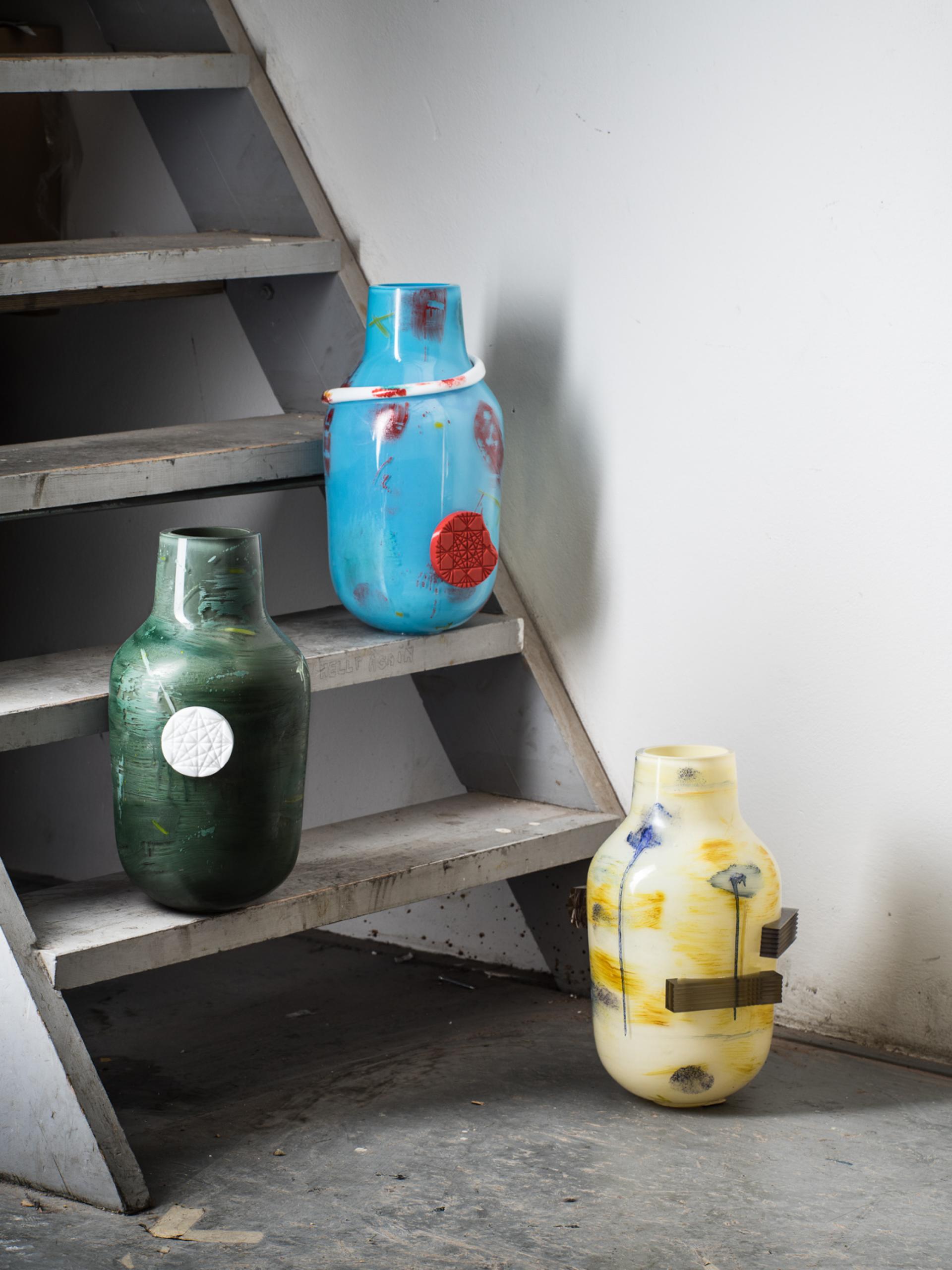 Colorful glass vases in various shapes displayed on a staircase, showcasing contemporary glass design at the London Design Fair.