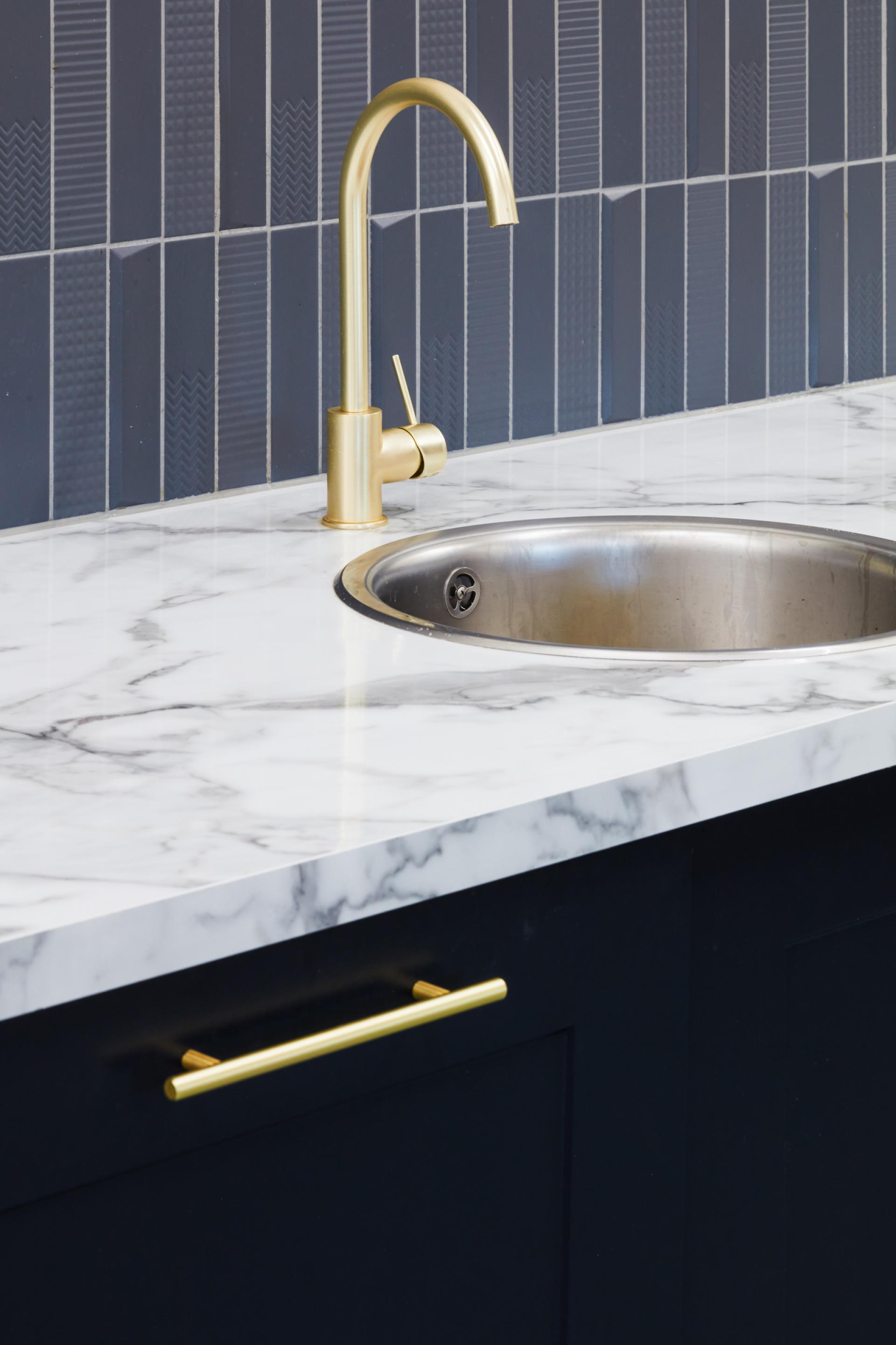 Stylish kitchen sink area featuring a gold faucet, marble countertop, and dark cabinetry, reflecting modern design principles.