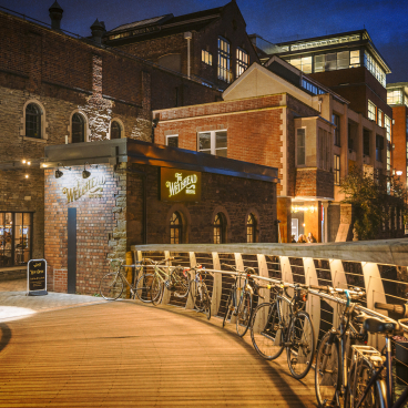 Welcoming entrance of The Wellhead bar in Bristol, featuring cosy lighting, bicycles, and historic architecture at night.