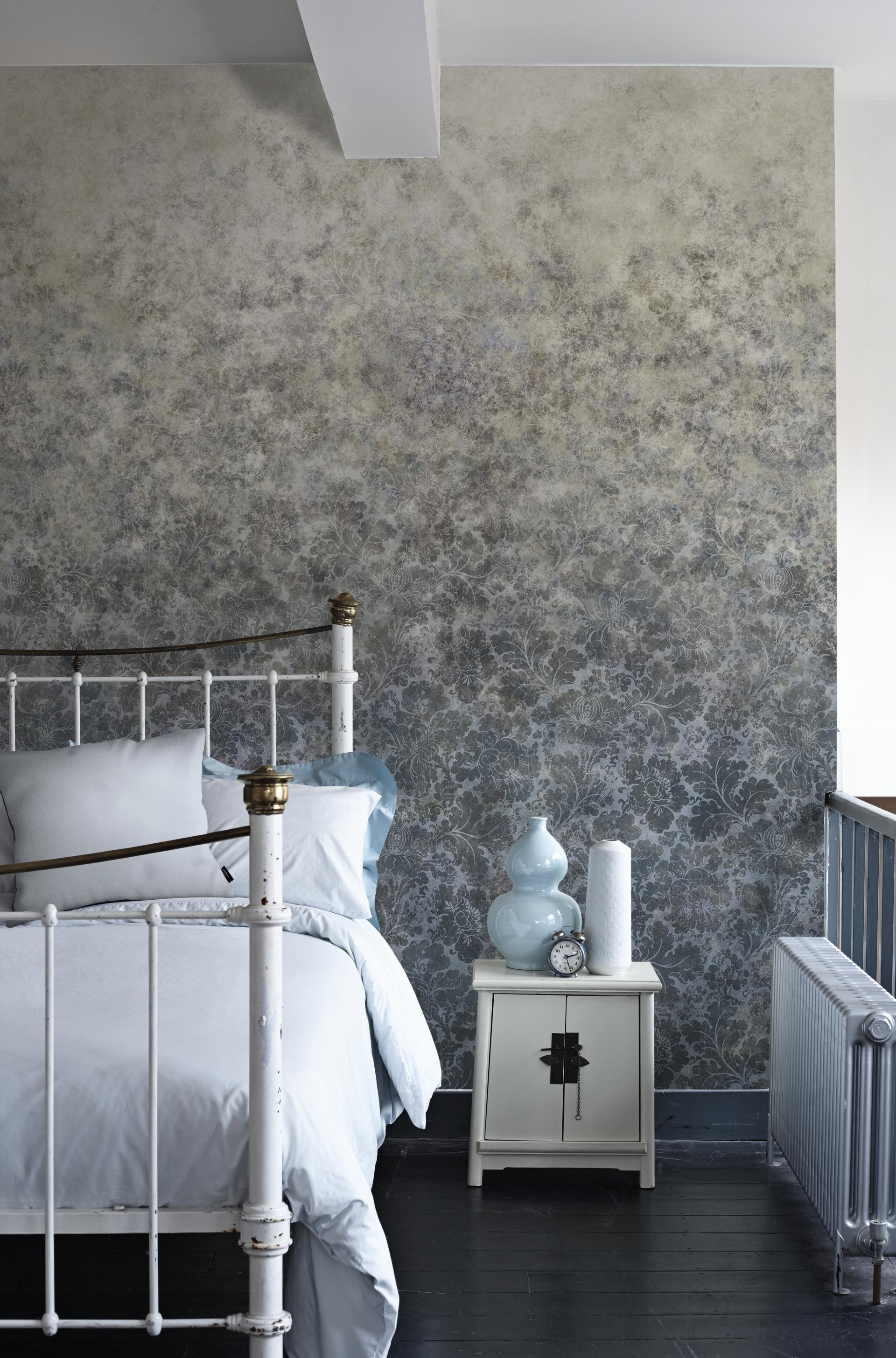 Elegant bedroom featuring V&A floral wallpaper, vintage bed, and stylish decor including a blue vase and bedside clock.