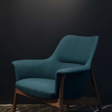 Stylish teal armchair with wood legs, showcasing Dare Studio's elegant British craftsmanship against a dark backdrop.