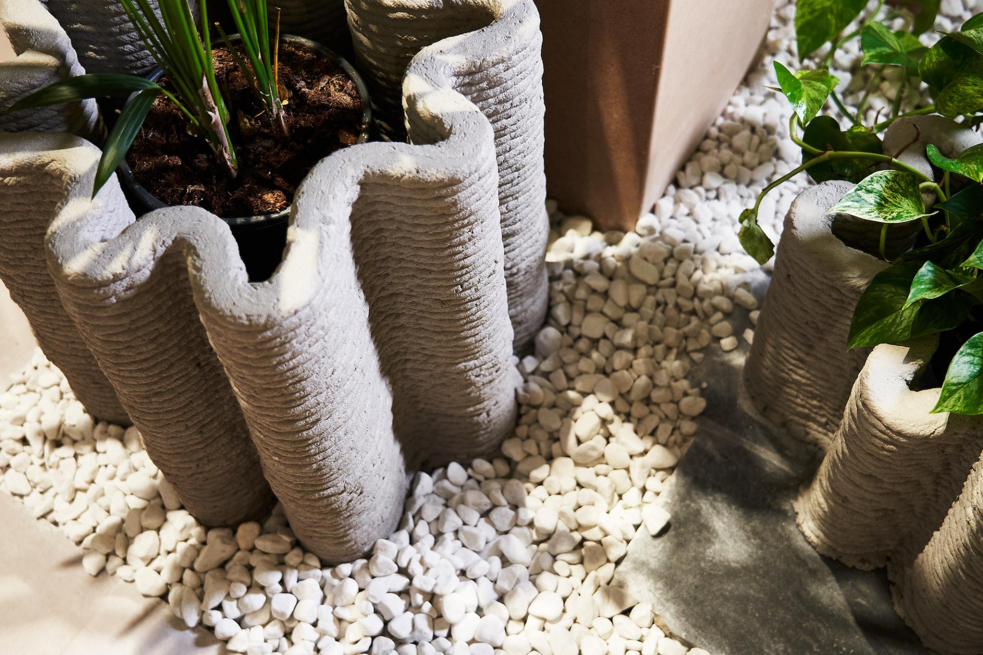 Textured concrete planters with greenery, placed on a bed of white stones at Material Source Studio in Manchester.