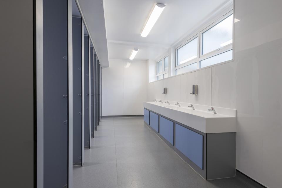 Modern boys' washroom with multiple sinks, blue cabinetry, and ample natural light at Stretford Grammar School.