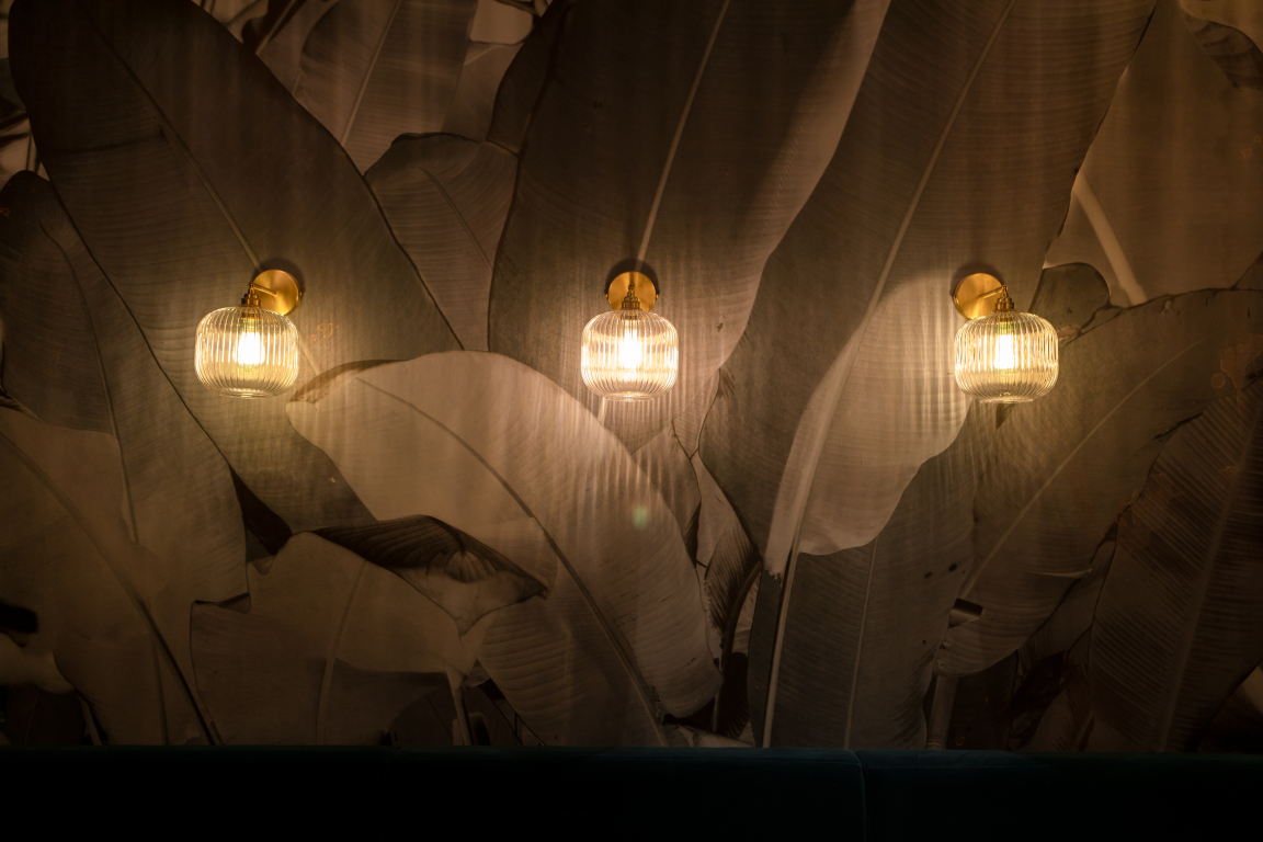 Elegant wall lights illuminate a tropical-themed space with large leaf patterns, enhancing the design ambiance.