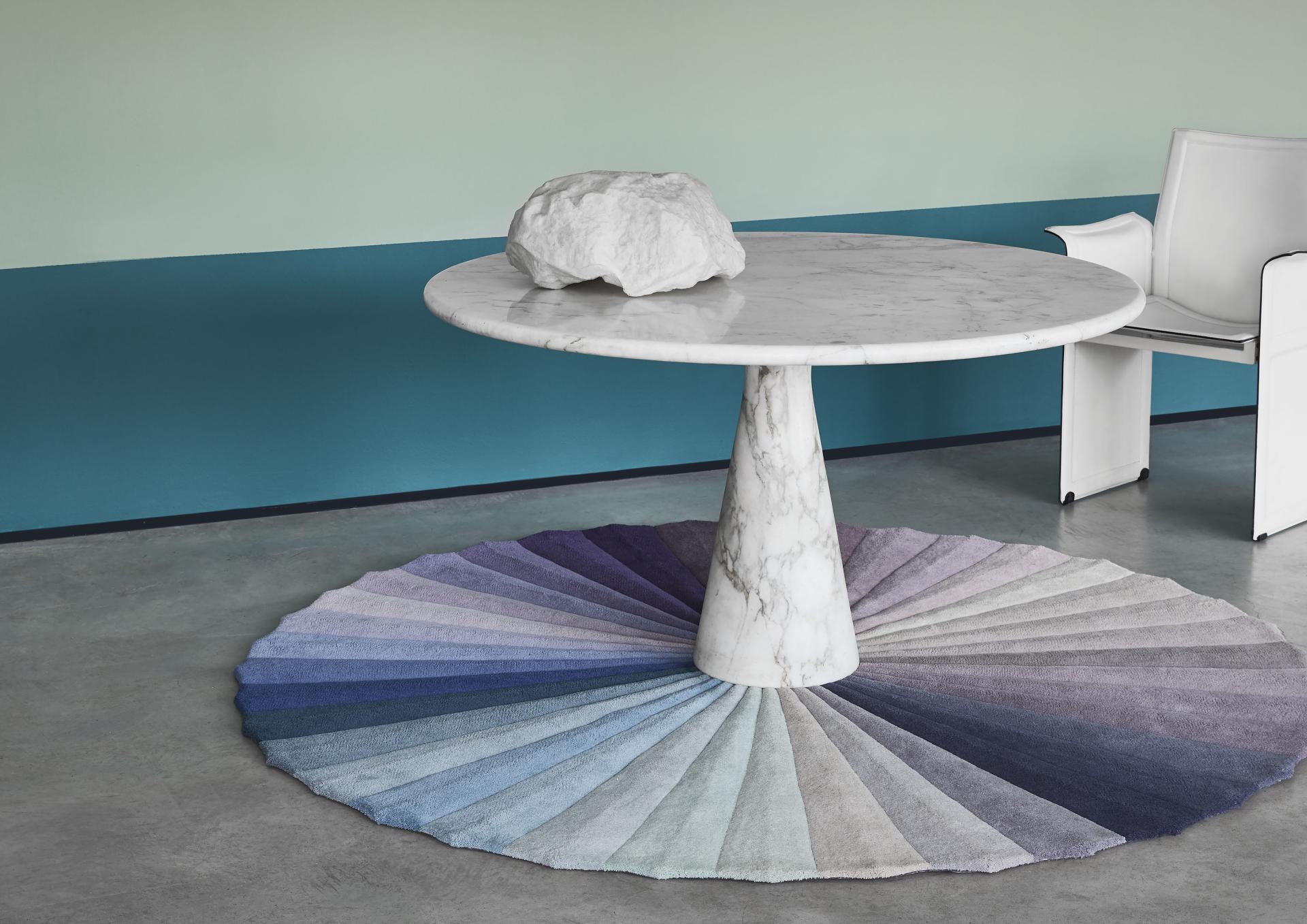 A modern dining table with a marble top, surrounded by a color-gradient rug, showcasing Kitty Joseph's collaboration with FLOOR_STORY.