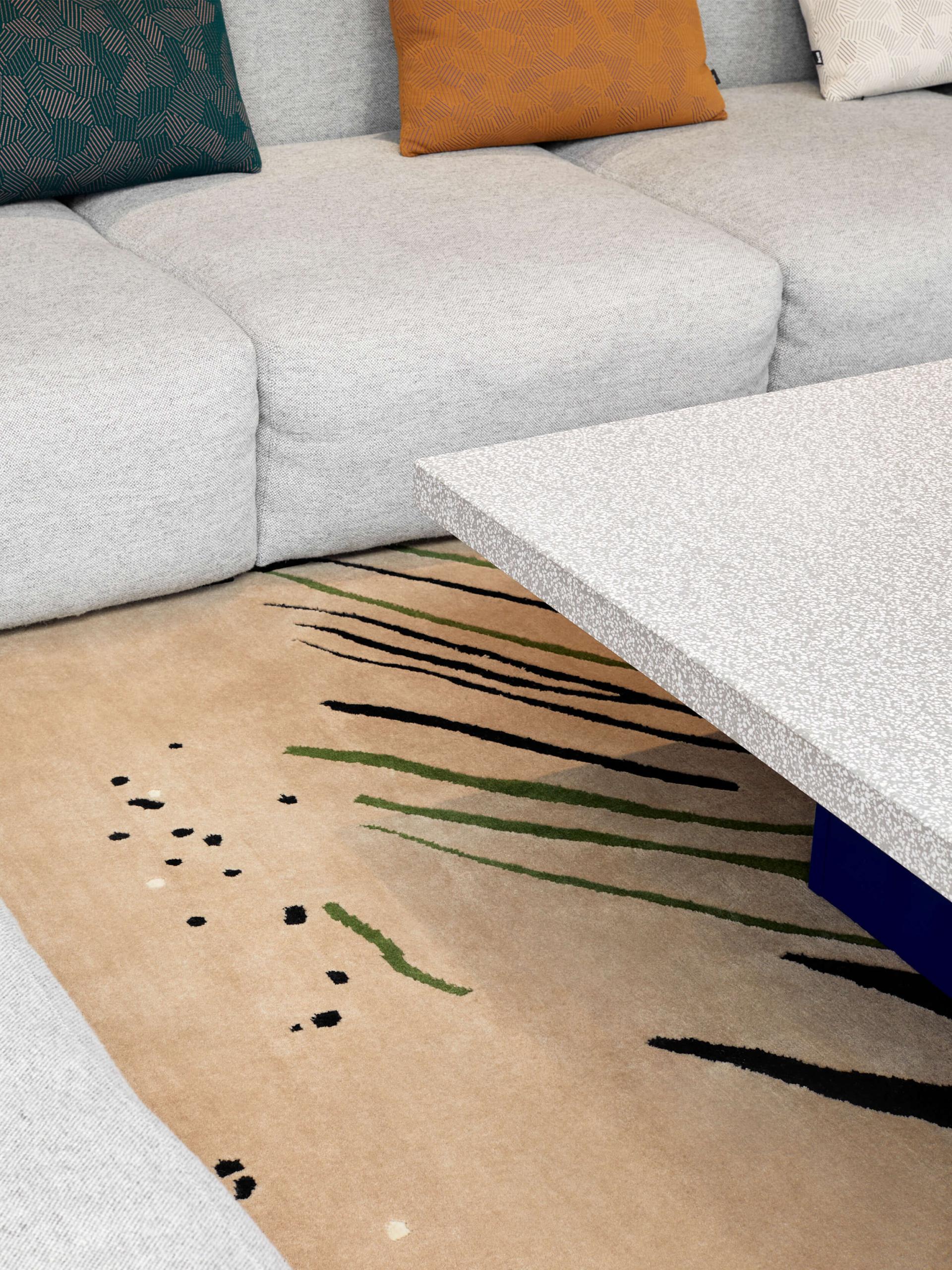 Contemporary lounge area featuring a textured grey sofa, colorful cushions, and an artistic rug with natural motifs.