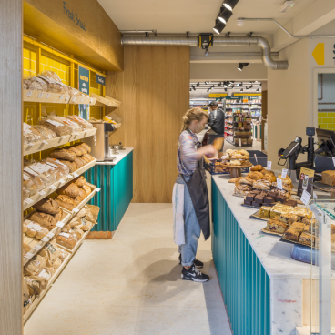 Brightly designed café-deli featuring fresh bread and baked goods, showcasing Better Food's new Gloucester Road store layout.