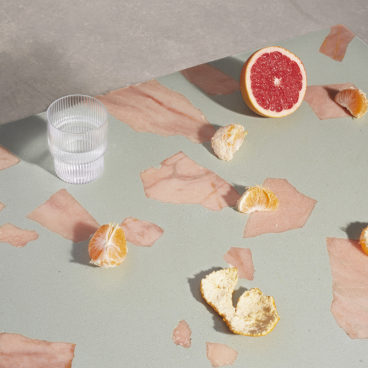 Colorful citrus fruits and a glass of water arranged on a surface featuring Altrock's innovative 2,000-year-old material.