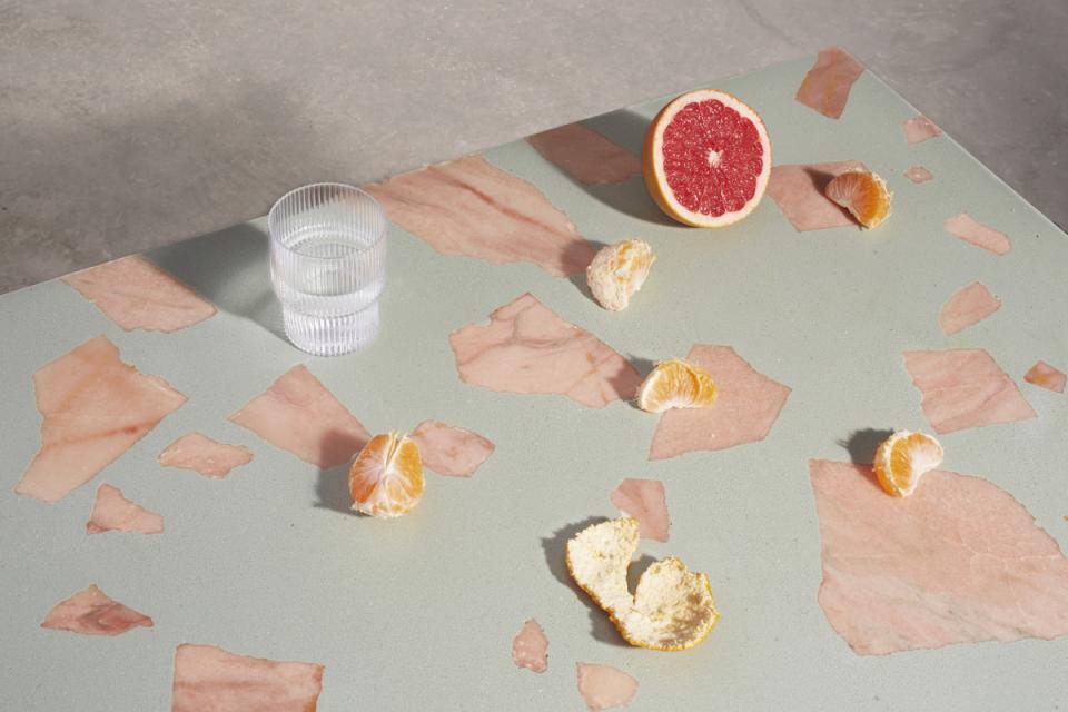 Colorful citrus fruits and a glass of water arranged on a surface featuring Altrock's innovative 2,000-year-old material.