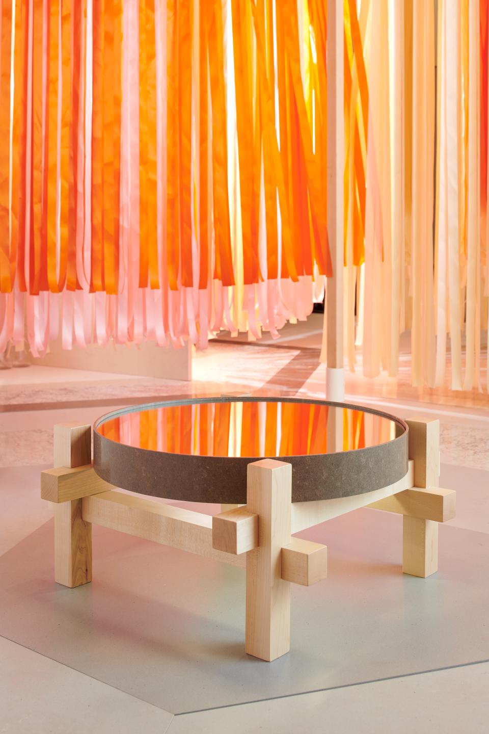 Contemporary round table designed by Marije Vogelzang, featuring a mirrored top and wooden base, against a colorful ribbon backdrop.