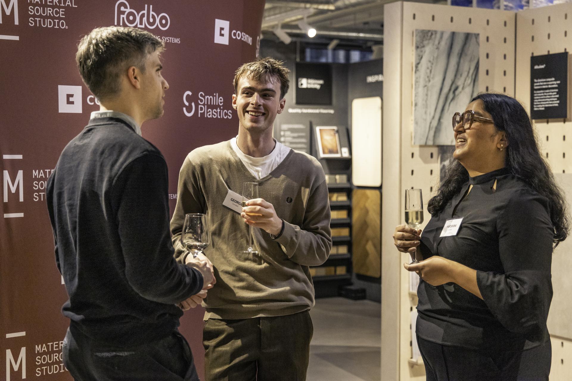 Professionals networking at a workplace technology event, discussing innovations with drinks in hand, surrounded by modern materials.