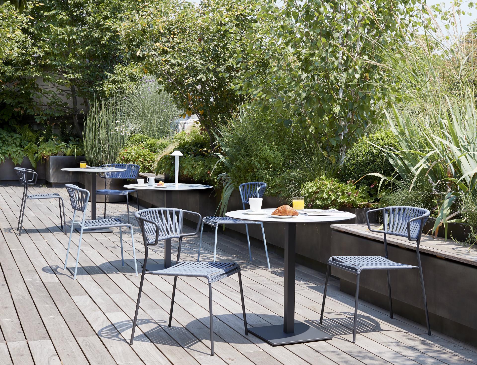 Stylish Lisa Club chairs by SCAB Design arranged around a modern outdoor dining table surrounded by lush greenery.