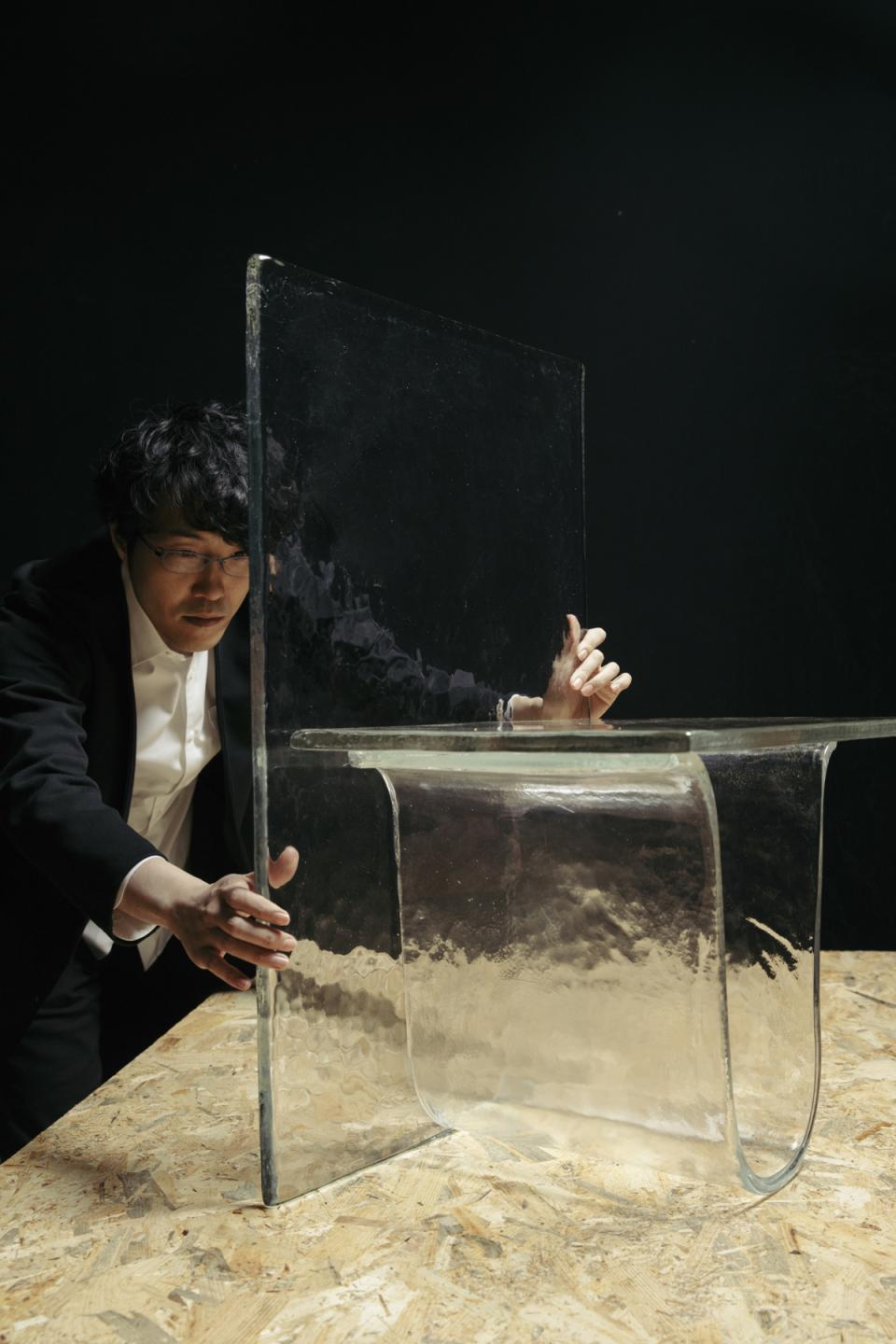 A designer carefully adjusts a Melt cast glass furniture piece, showcasing its transparent, fluid form against a dark background.