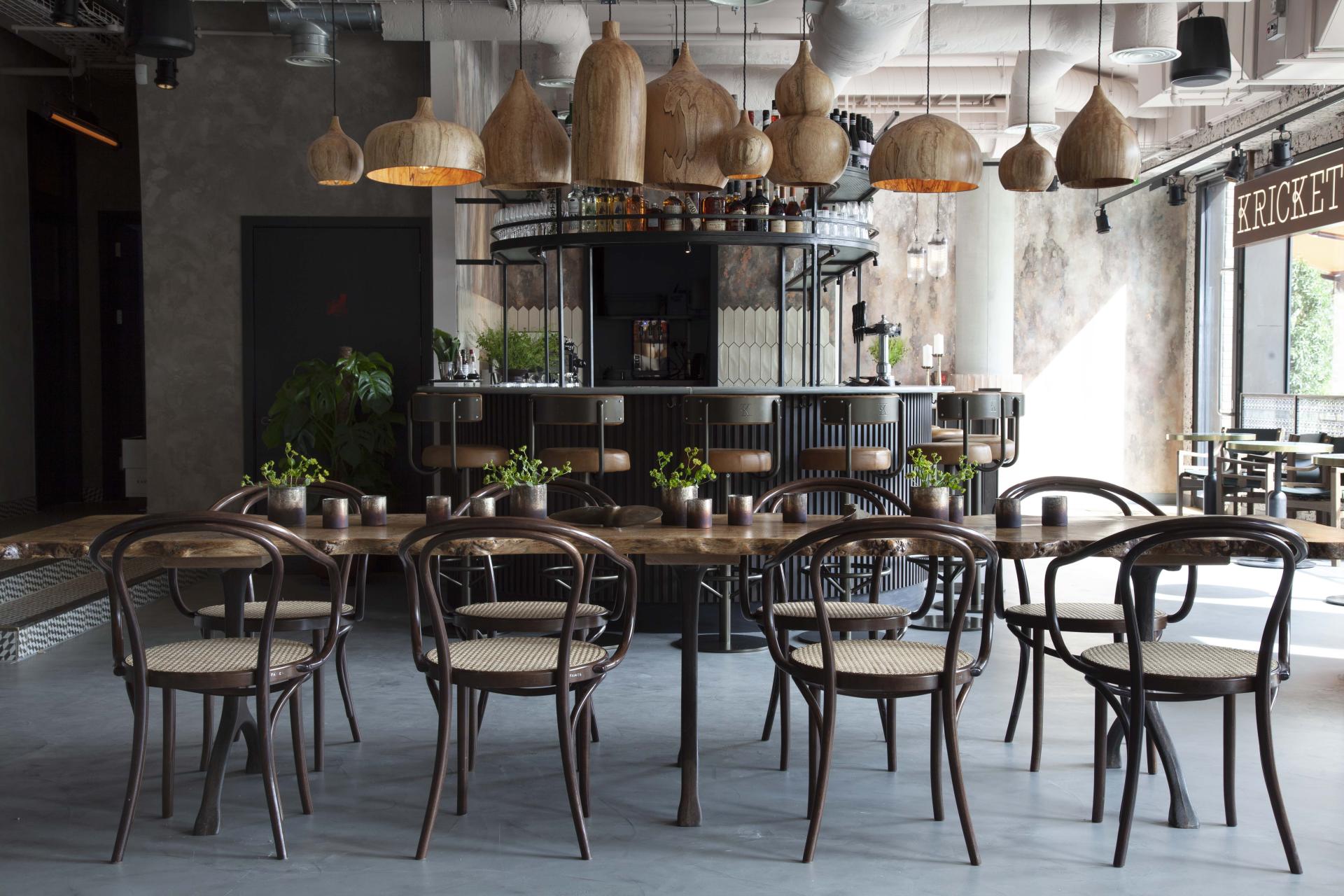 Stylish interior design of Kricket TVC restaurant featuring wooden tables, unique lighting, and a chic bar area.